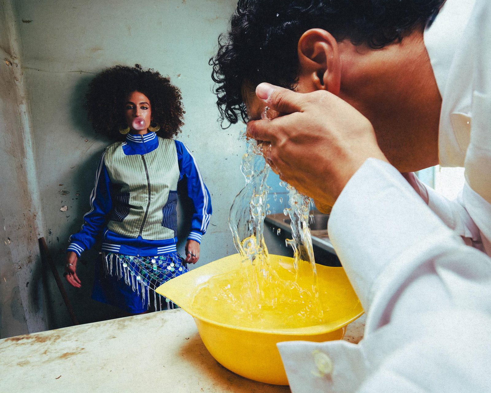 Two models at a washbasin, water pouring into a yellow bowl