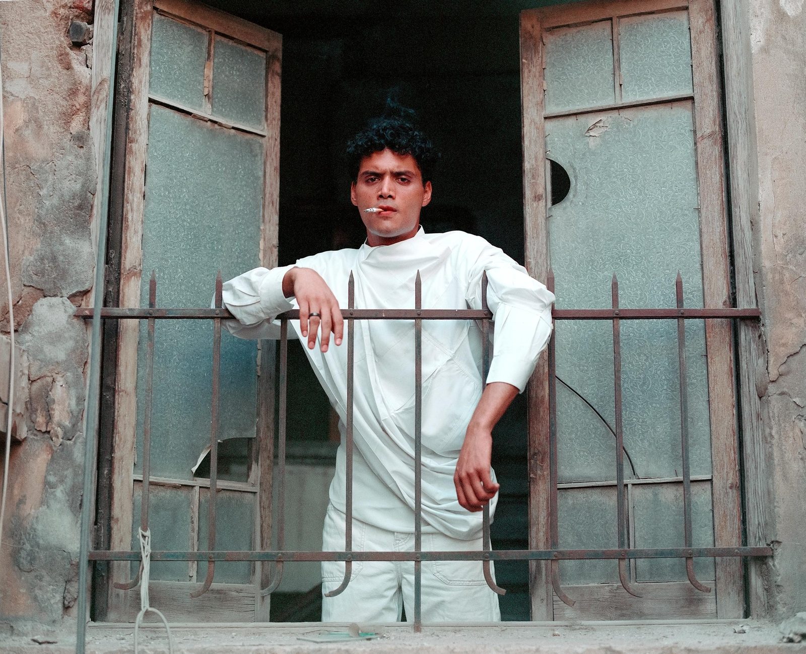 Model in white leaning on an iron window grille
