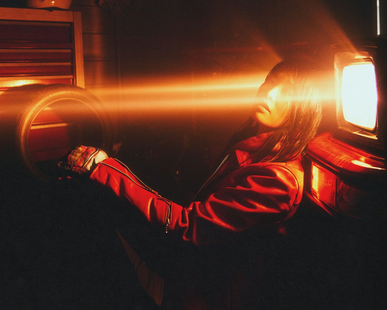 Model in a red leather jacket lit by a horizontal flare of warm light in a dark garage