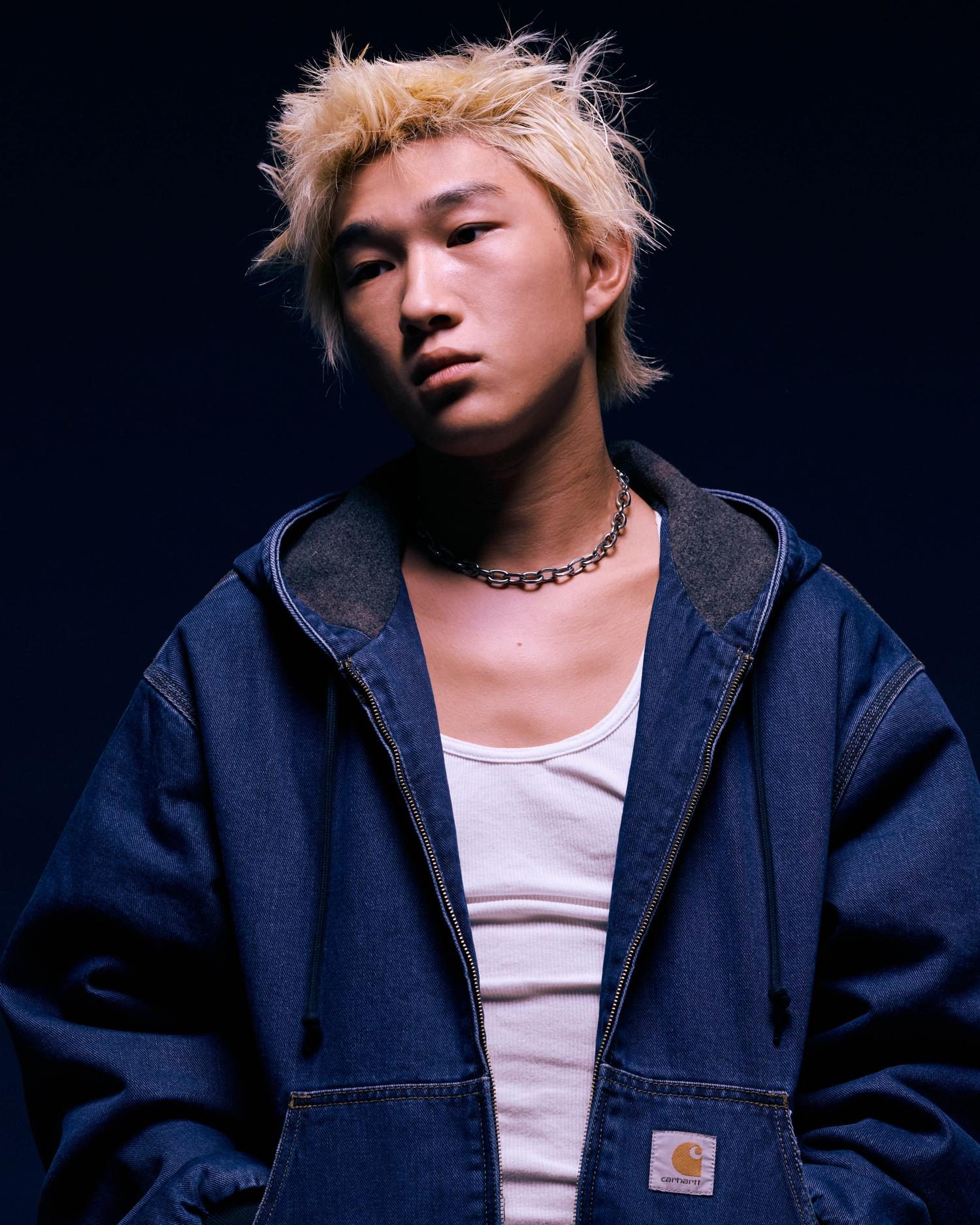 Studio portrait of a blond model in a dark denim Carhartt hooded jacket with a chain necklace
