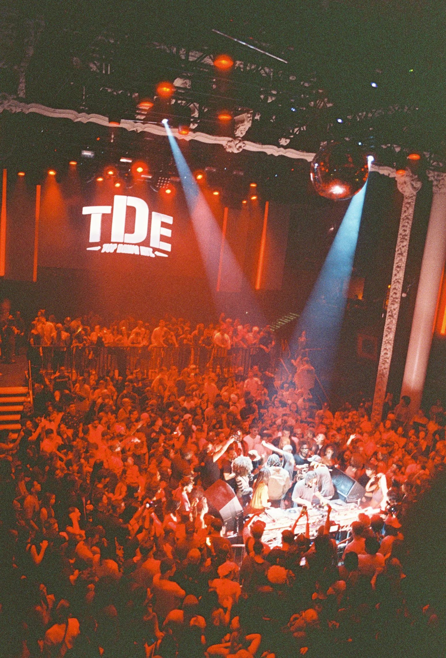 TDE logo projected above a red-lit club crowd under a mirror ball