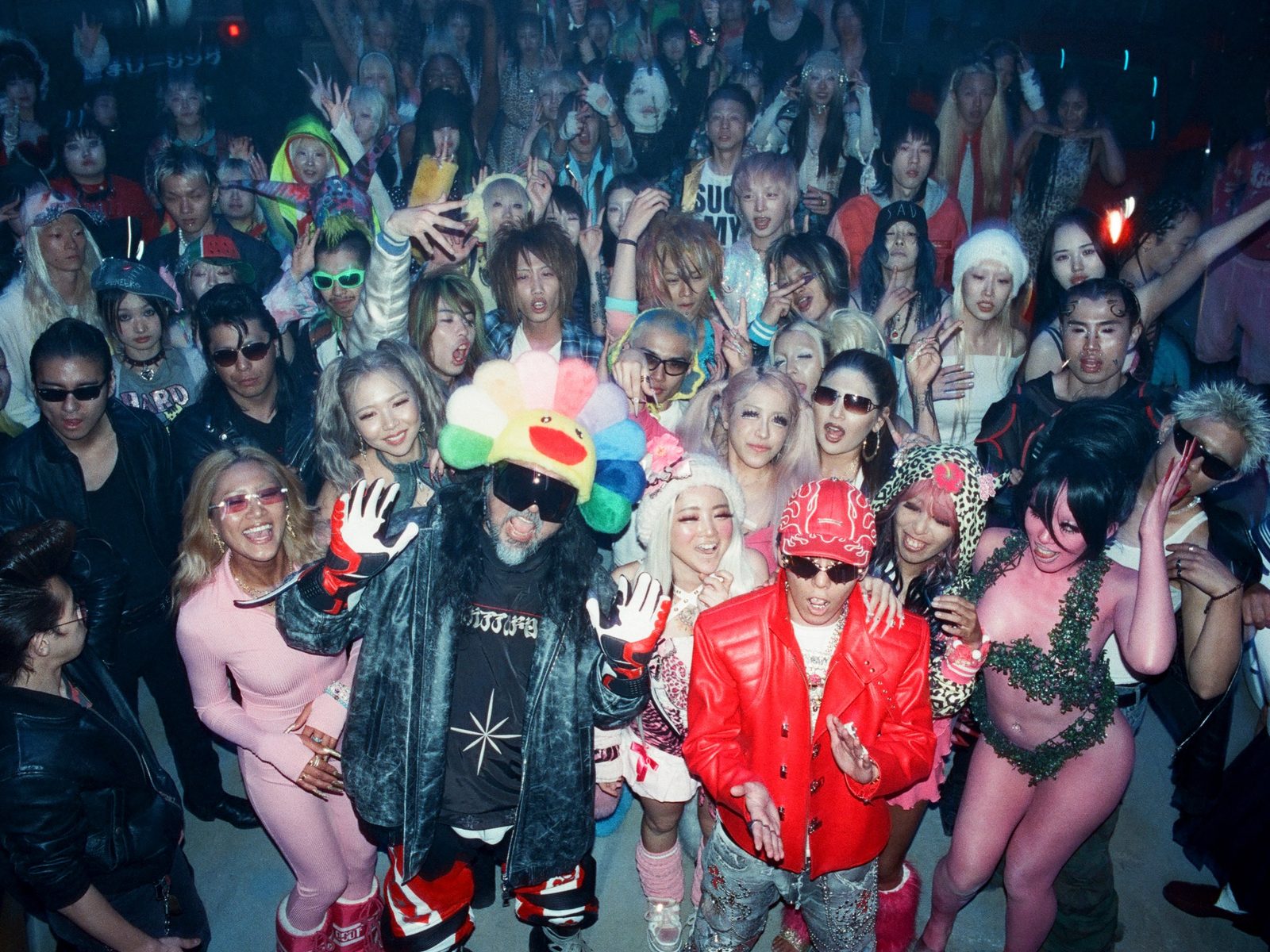 Takashi Murakami in a flower-petal hat surrounded by a dense Tokyo club crowd, shot on flash film