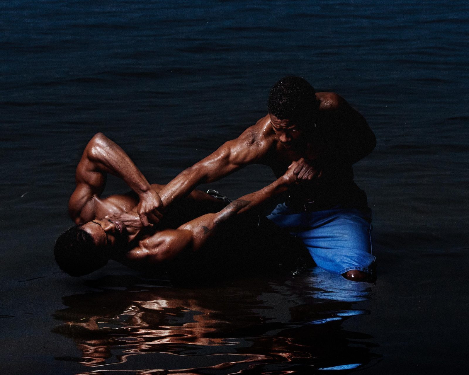 Two men wrestling waist-deep in dark water at night