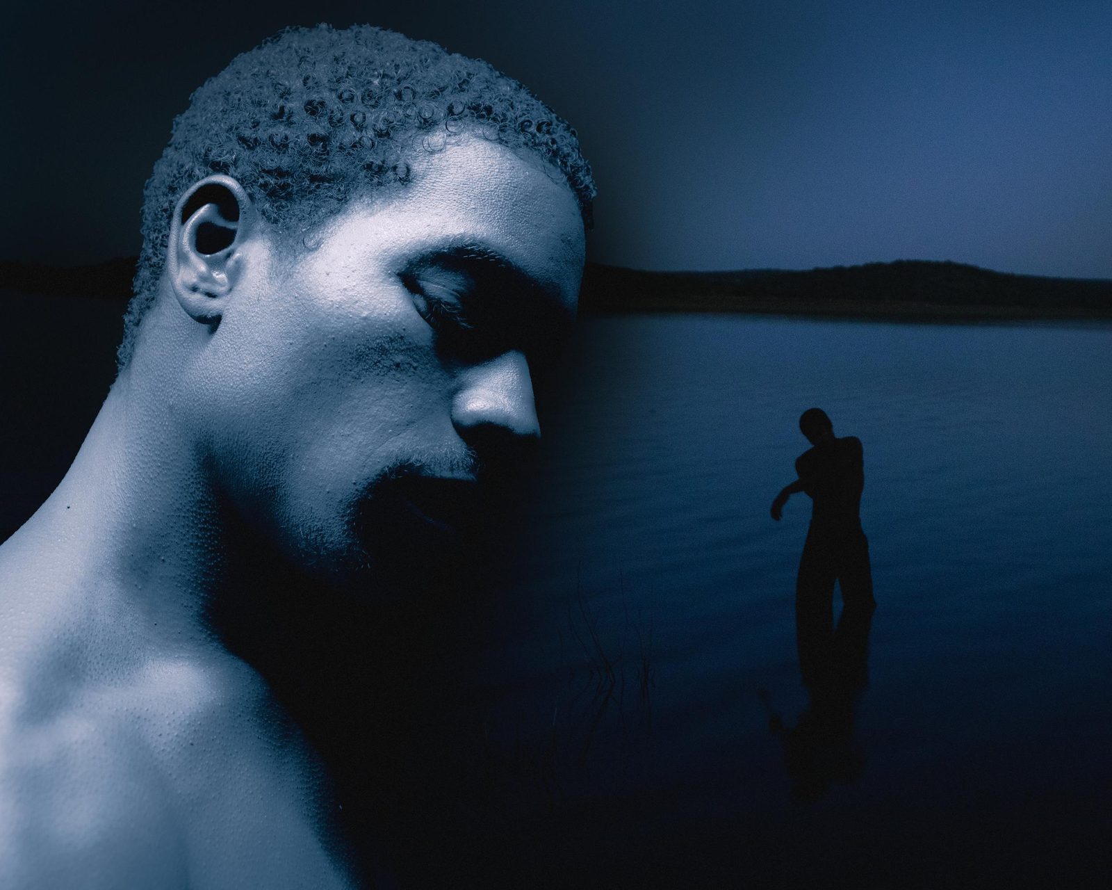 Blue night double exposure: a close profile with eyes closed over a silhouette standing in still water